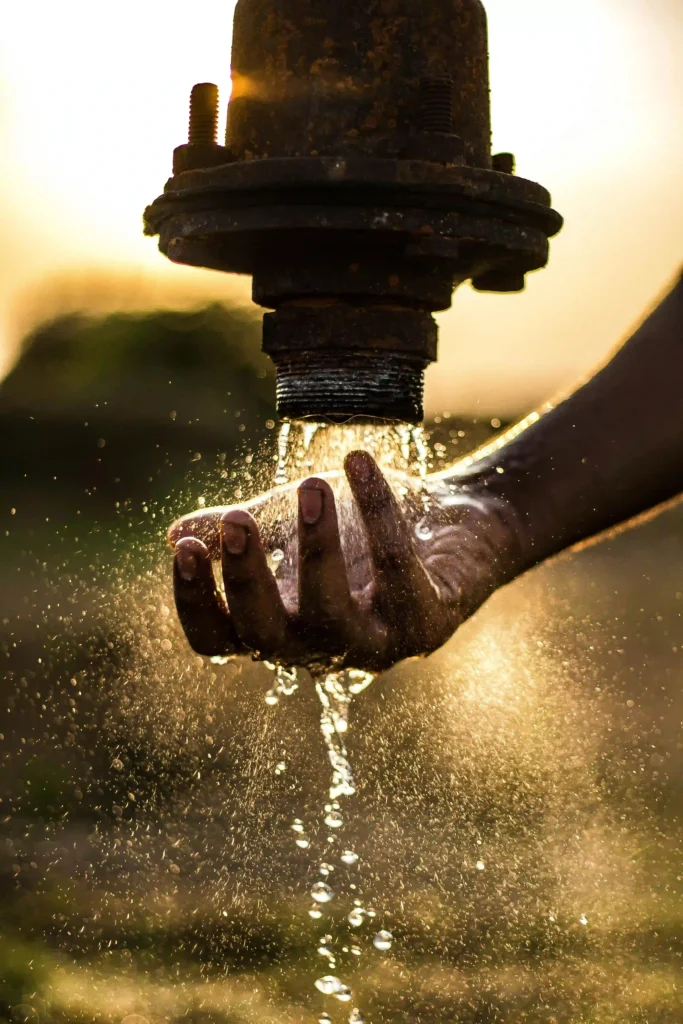 Clean water flowing from pipe into a person's hand at sunset representing access to safe drinking water